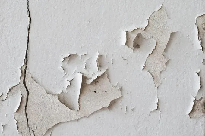 Textured wall with peeling paint and cracks revealing a lighter surface underneath.